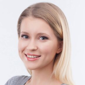 A young woman with long blonde hair smiles at the camera. She is wearing light makeup and a light-colored top. The background is plain and white.